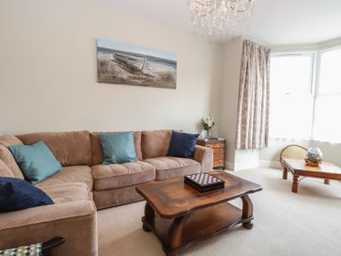 A living room with a beige sofa and blue cushions a wooden coffee table and a side table with flowers at 34 North Denes Road in Great Yarmouth