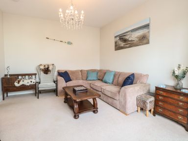 A living room with a beige corner sofa and blue cushions a wooden coffee table and an armchair at 34 North Denes Road Great Yarmouth