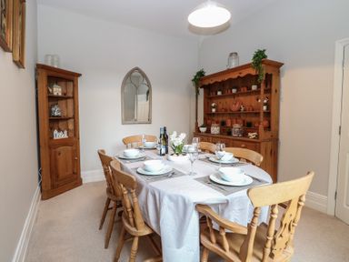 A dining room with a wooden table set with white dishes and glassware six wooden chairs wooden cabinets and a wall mirror at 34 North Denes Road in Great Yarmouth