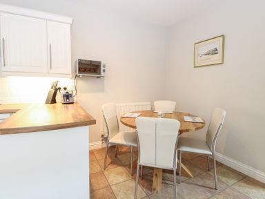 A kitchen area with wooden countertop a toaster knife block round wooden dining table four chairs and a framed picture on the wall at 34 North Denes Road in Great Yarmouth