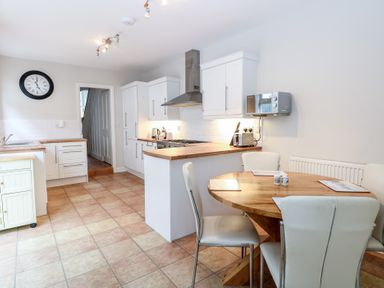 A kitchen with white cabinets wooden countertops a round wooden dining table with white chairs and a wall clock at 34 North Denes Road in Great Yarmouth