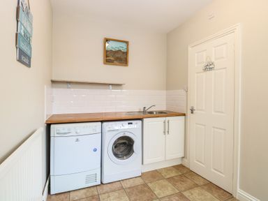 A utility room with a washing machine dryer under a wooden countertop and a sink near a closed door at 34 North Denes Road in Great Yarmouth