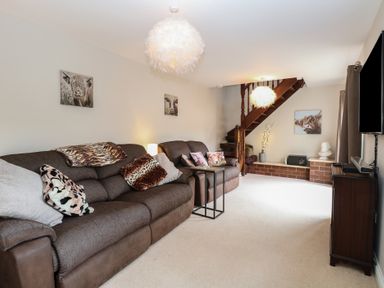 A living room with two brown sofas animal print cushions a small black side table wooden stairs and wall art at 34 North Denes Road in Great Yarmouth