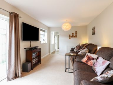 A living room with a sofa with animal print cushions a wall-mounted television and a wooden cabinet at 34 North Denes Road in Great Yarmouth