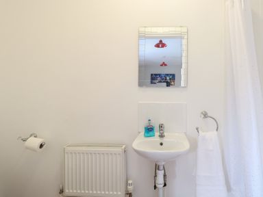 A bathroom with a wall-mounted sink a mirror a radiator a towel ring with a towel and a toilet paper holder at 34 North Denes Road in Great Yarmouth
