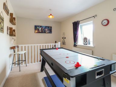 A game room with an air hockey table a bar stool a window with curtains and wall decorations at 34 North Denes Road in Great Yarmouth