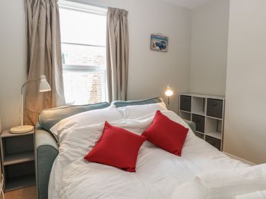 A bedroom with a sofa bed opened with white bedding and red cushions near a window at 34 North Denes Road in Great Yarmouth
