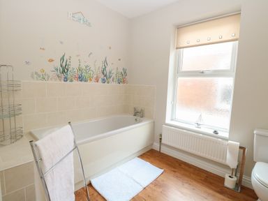 A bathroom with a bathtub wall tiles a window radiator towel rail and toilet at 34 North Denes Road Great Yarmouth
