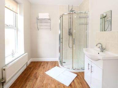A bathroom with a curved glass shower, white sink cabinet, towel rack, and wooden floor at 34 North Denes Road in Great Yarmouth