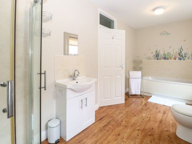 A bathroom with a shower, sink, bathtub with sea life wall decals, towel rack, and wooden floor at 34 North Denes Road in Great Yarmouth