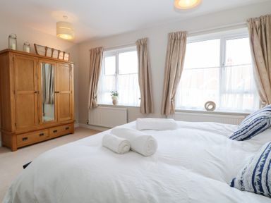 A bedroom with a wooden wardrobe folded towels on a bed and windows with curtains at 34 North Denes Road in Great Yarmouth
