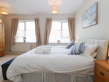 A bedroom with a double bed pillows and rolled towels by two windows with curtains at 34 North Denes Road in Great Yarmouth