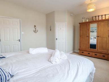 A bedroom with a bed with white linens two doors a wooden wardrobe and a wall decoration at 34 North Denes Road Great Yarmouth