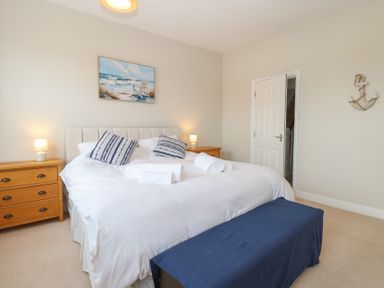 A bedroom with a double bed and striped pillows two bedside tables with lamps and a painting of a beach above the bed at 34 North Denes Road in Great Yarmouth