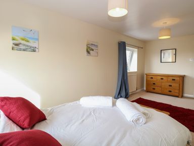 A bedroom with a bed with red pillows and white towels a wooden dresser a red rug and two paintings on the wall at 34 North Denes Road in Great Yarmouth