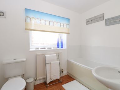 A bathroom with a toilet towel rack bathtub sink and window with a printed blind at 34 North Denes Road in Great Yarmouth