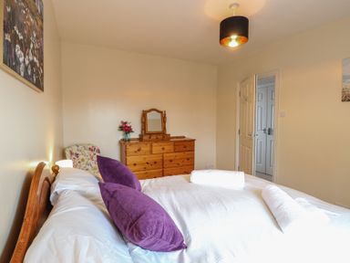 A bedroom with a bed with purple pillows and white towels a wooden dresser with a mirror and a floral chair at 34 North Denes Road Great Yarmouth