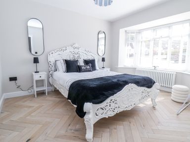 A bedroom with a carved white bed frame black pillows bedside tables with lamps and two oval mirrors near large windows at Ty Blodau near Prestatyn