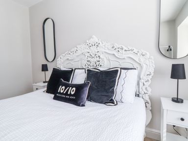 A bedroom with an ornate white headboard black pillows black lamps and two mirrors at Ty Blodau near Prestatyn