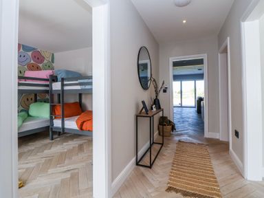 A hallway with a narrow table and round mirror next to a room with bunk beds and colorful bedding at Ty Blodau near Prestatyn