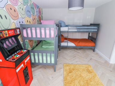 A bedroom with two gray bunk beds a red arcade machine and a yellow rug at Ty Blodau near Prestatyn