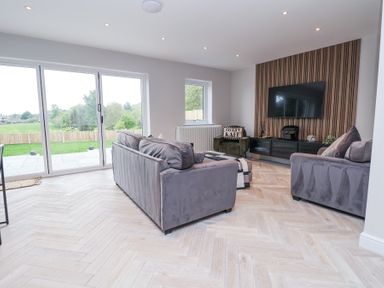 A living room with two gray sofas a green armchair a television mounted on a wooden panel and large glass doors at Ty Blodau near Prestatyn