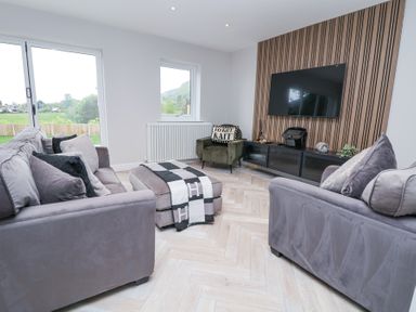 A living room with two sofas a chair ottoman and a wall-mounted television at Ty Blodau near Prestatyn