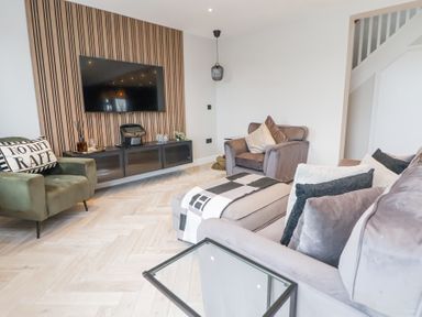 A living room with velvet armchairs a wall-mounted TV and a wooden slat panel at Ty Blodau near Prestatyn