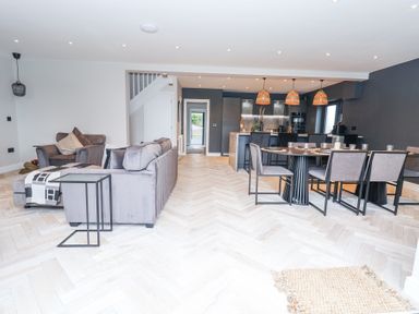 An open plan living room and dining area with grey sofas and chairs a dining table with chairs and hanging lamps at Ty Blodau near Prestatyn