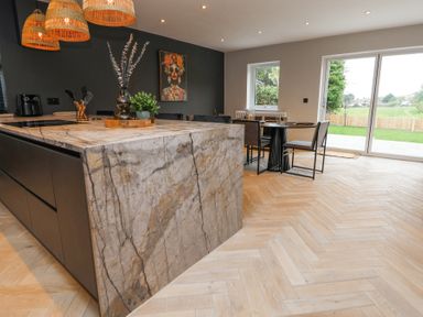 A kitchen with a marble island black cabinets a dining table with chairs and large glass doors at Ty Blodau near Prestatyn