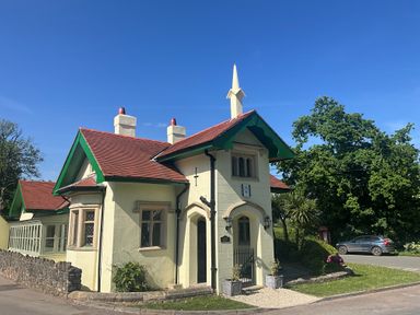 A small cream-colored house with a red roof and green trim near a road with a parked car and trees at Hafod Lodge in Hensol near Pontyclun