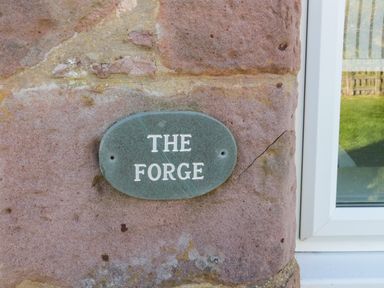 A green oval plaque with the words The Forge on a stone wall next to a white window at The Forge in Nr Seashouses