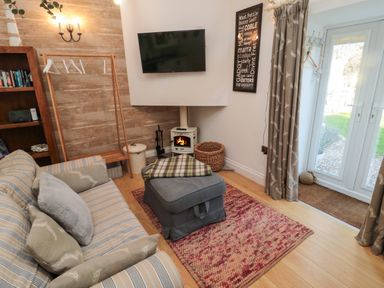A living room with a striped sofa, ottoman, fireplace, mounted TV, and glass doors at The Forge in Nr Seabouses