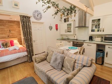 A small living area with a striped sofa beside a kitchen and a bed partially hidden by curtains at The Forge in Nr Seashouses