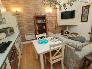 A small open plan kitchen and living area with striped sofas a dining table and chairs a wood stove and a wall mounted tv at The Forge in Nr Seabouses