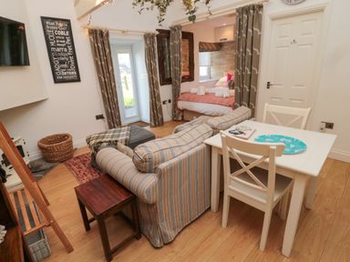 A living room with a striped sofa a small white dining table and chairs a bed area separated by curtains and wall decor at The Forge in Nr Seabhouses