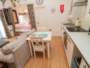 A kitchen and dining area with a striped sofa and a bed visible through curtains at The Forge Nr.Seahouses