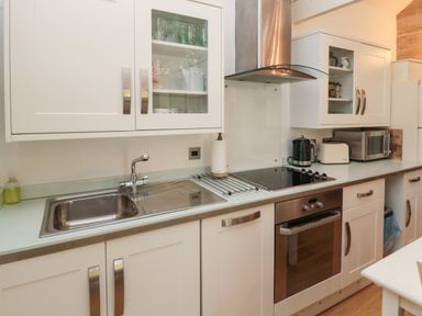 A kitchen with a sink stove oven microwave toaster kettle and white cabinets at The Forge in Nr.Seahouses