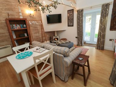 A living room with a striped sofa small dining table wooden bookshelf wall mounted tv and double doors at The Forge Nr Seauhousess