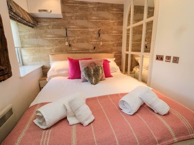 A bedroom with a bed with pink pillows and a heart-shaped pillow and rolled white towels on a striped pink blanket at The Forge in Nr Seashouses