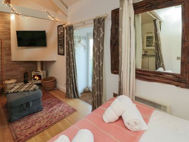 A bedroom with a wooden-framed mirror towels on bed a small stove television and a window at The Forge Nr.Seahouses