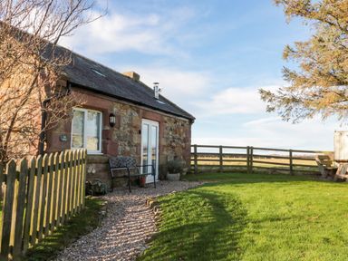 A stone cottage with a bench and gravel path in a fenced yard at The Forge Nr.Seahouses
