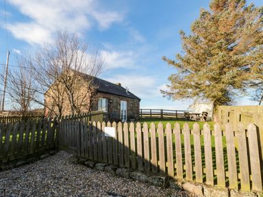 A small stone house with a fenced grassy yard and outdoor bench and table at The Forge in Nr Seashouses
