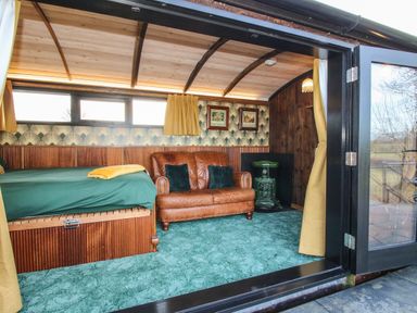 An interior room with a brown leather sofa a green carpet a bed with green bedding and yellow curtains at GWR Wagon - Victoria Station Ludlow