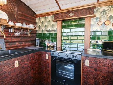 A kitchen with dark brown cabinets a black oven green tiled backsplash and open wooden shelves at GWR Wagon - Victoria Station in Ludlow