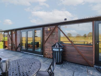 An outdoor patio area with a round metal table and chairs next to a wooden building with large windows and glass doors at GWR Wagon Victoria Station Ludlow