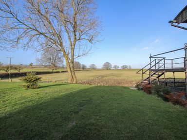 A grassy backyard with a bare tree and metal stairs overlooking open fields at GWR Wagon - Victoria Station in Ludlow
