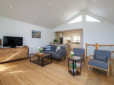 A living room with a sofa and two armchairs a wooden cabinet with a TV and a coffee table with plants at Jacana in Perranporth