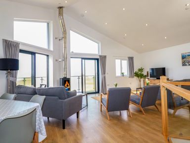 A living room with gray sofas a wood stove and dining table at Jacana in Perranporth