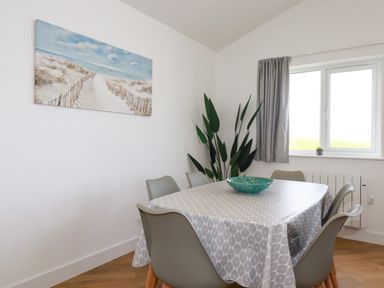 A dining room with a table covered with a patterned tablecloth and six gray chairs at Jacana in Perranporth